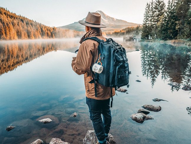 Gent overlooking the water, wearing backpack containing a mug and one of the best portable espresso makers