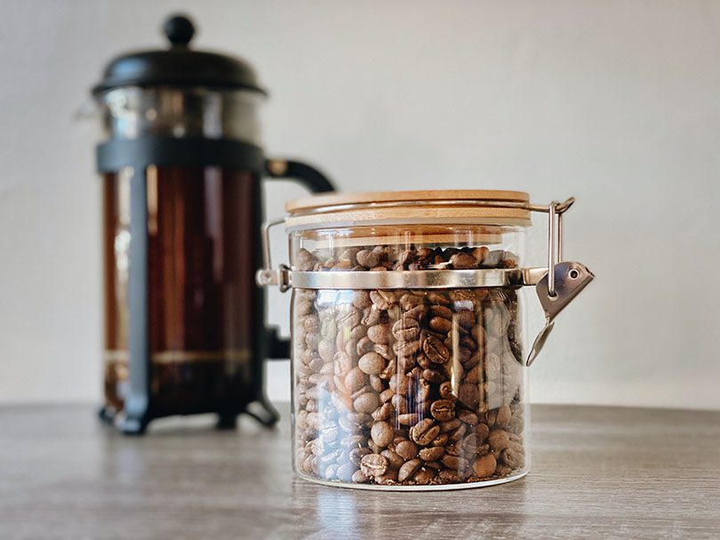 Jar of coffee beans in front of French press
