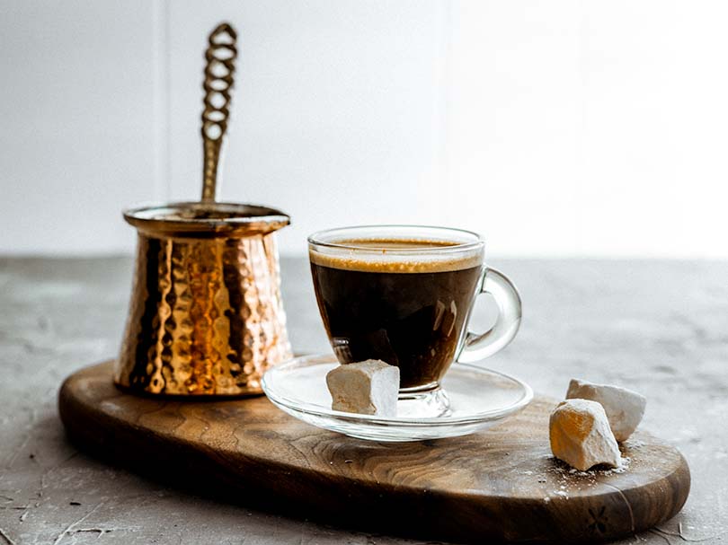 Ibrik (Turkish coffee maker) sitting on a board beside a cup of coffee and Turkish delight