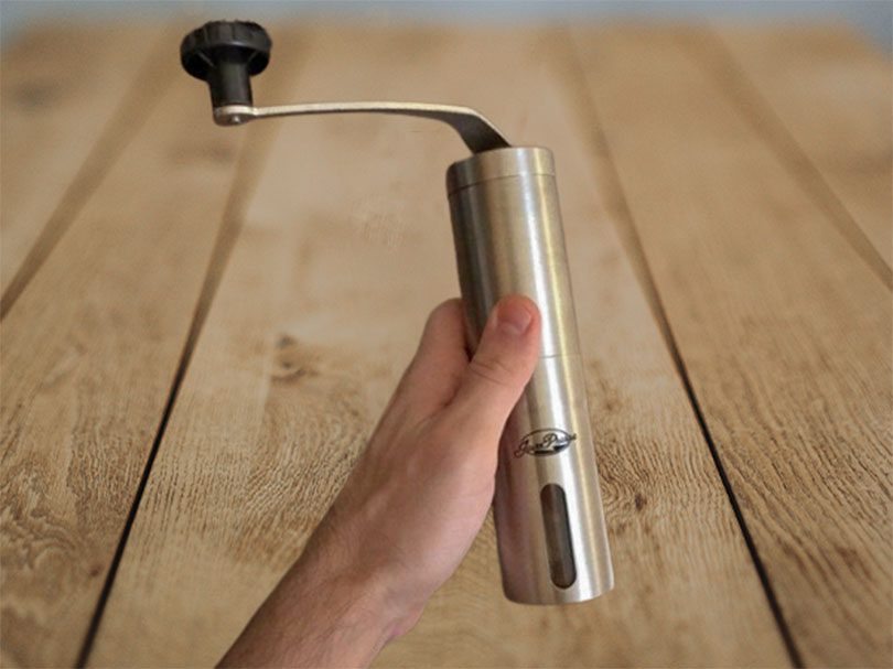 Hand holding the Javapresse manual coffee grinder over a wooden table