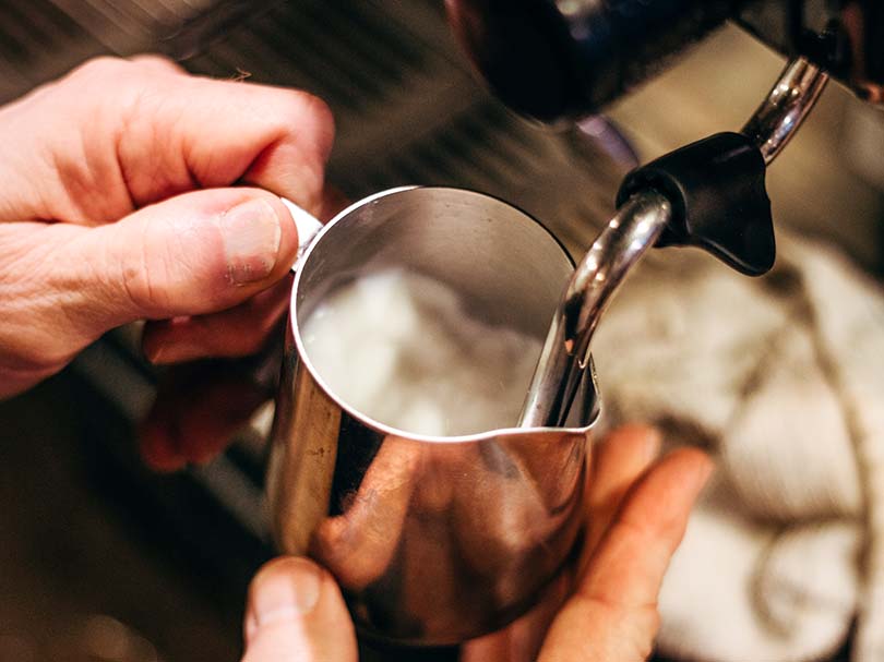 Milk frothing pitcher being used on the steam wand of an espresso machine