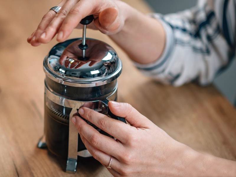 Hands pressing plunger on French press coffee maker