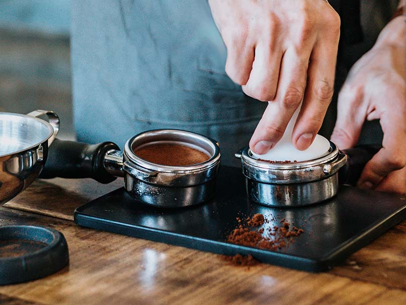 Portafilter with tamped coffee, and hands tamping another one