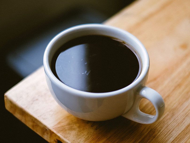 Cup of Americano coffee sitting on the edge of a wooden table