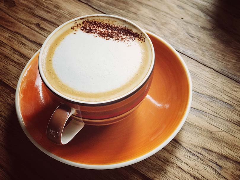 Cappuccino in orange cup/saucer, on a wooden table