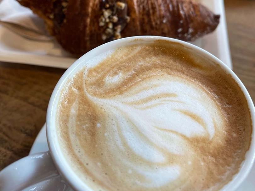Frothy cappuccino with a croissant behind it