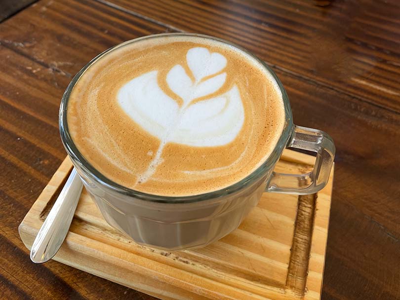 Flat white with basic latte art in a glass, sitting on a wooden board