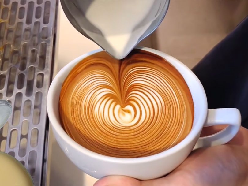 Making a kyoto latte with latte art, condensed milk sitting on the espresso machine's drip tray