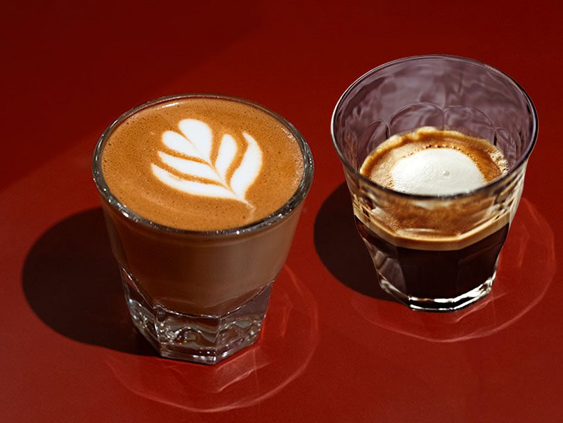 Cortado and espresso macchiato sitting side-by-side on a vibrant red table