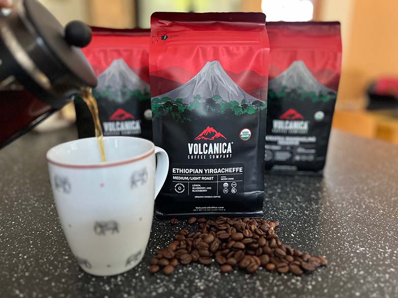 Three bags Volcanica Ethiopian Yirgacheffee with some of the coffee beans on the counter, French press being poured into mug