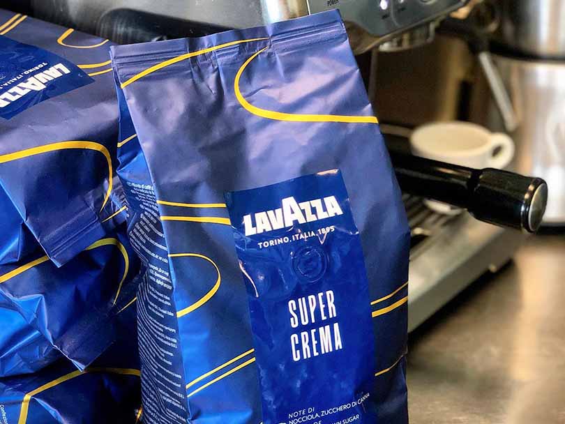 Bags of Lavazza Super Crema coffee beans with espresso machine in the background