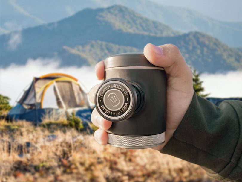 Holding the portable Wacaco Picopresso to the camera, tent and mountains in the background