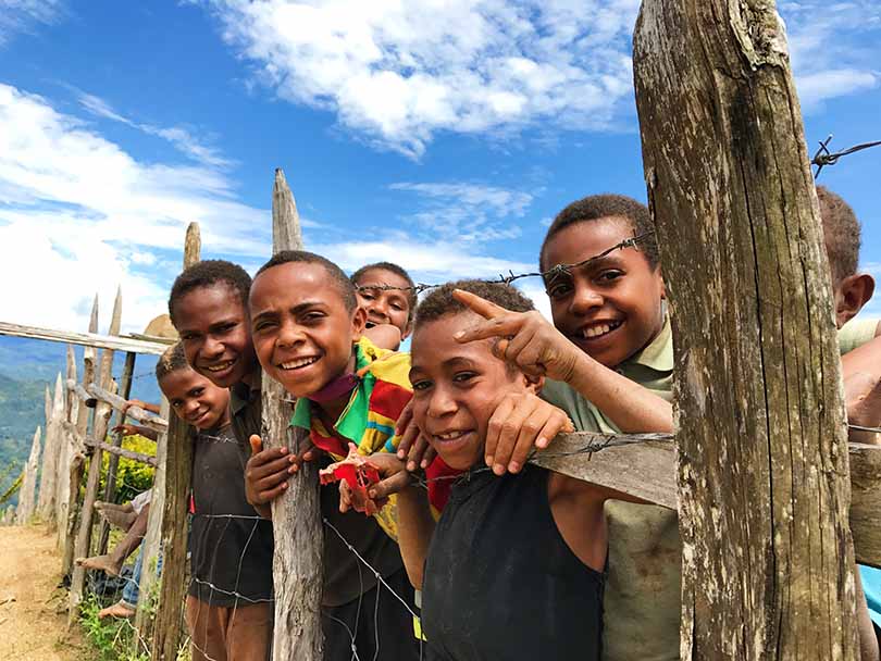 Children smiling from behind a fence on their coffee farm in Papua New Guinea