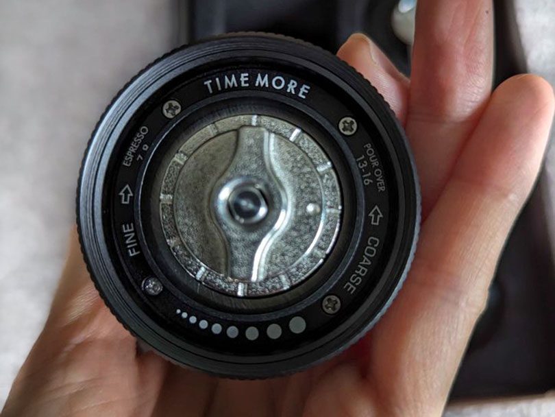 Hand holding the Timemore C3 grinder up to the camera, focused on the grind adjustment dial