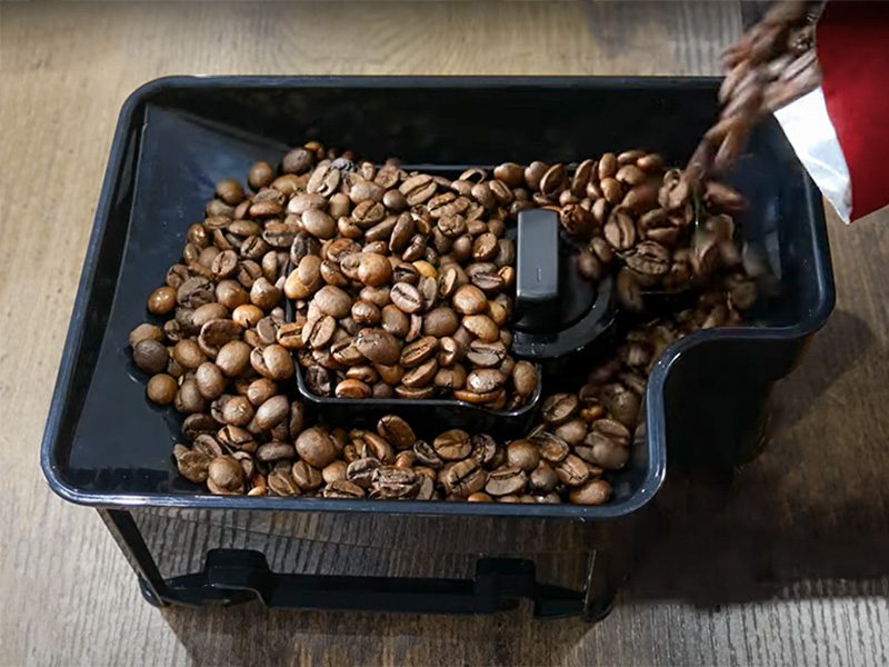 Pouring coffee beans into the refillable bean hopper of a KitchenAid super-automatic espresso machine